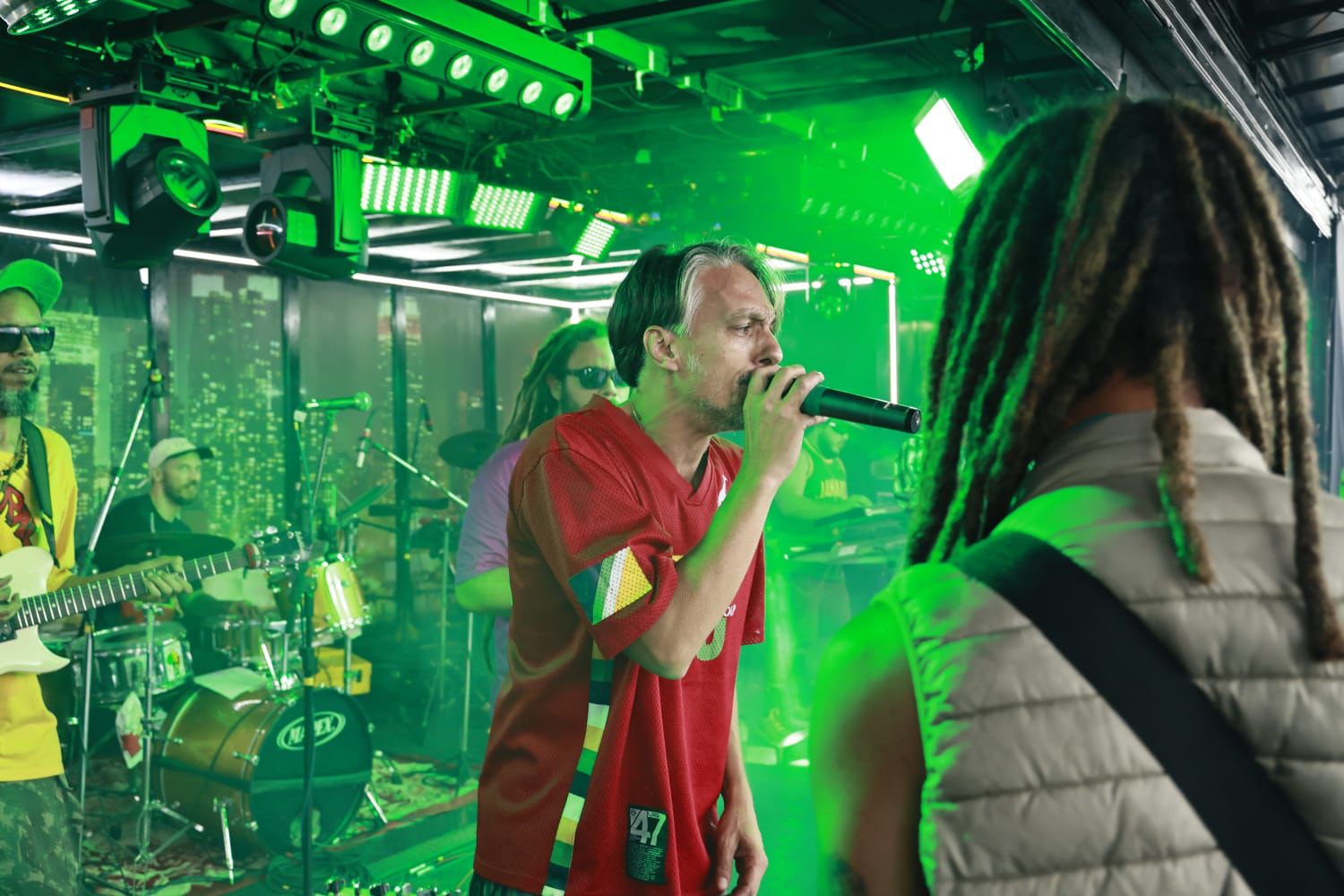 Brasil Riddim ao vivo sob iluminação verde intensa com vocalista de camisa vermelha